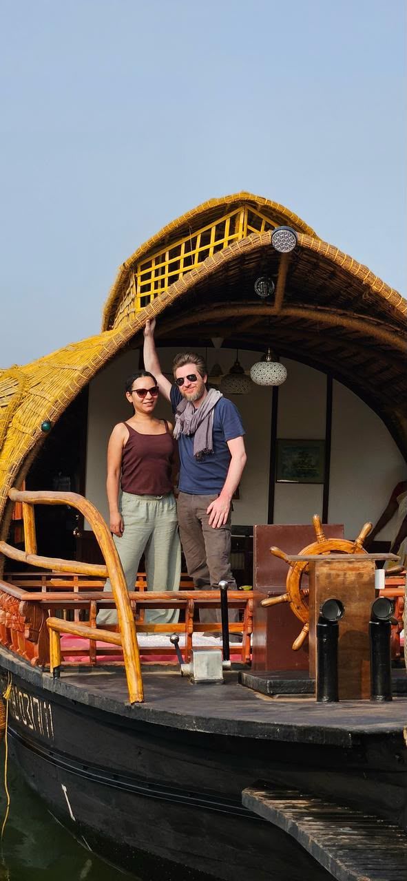 Two guests standing at the bow under the golden woven roof, next to the wooden steering wheel